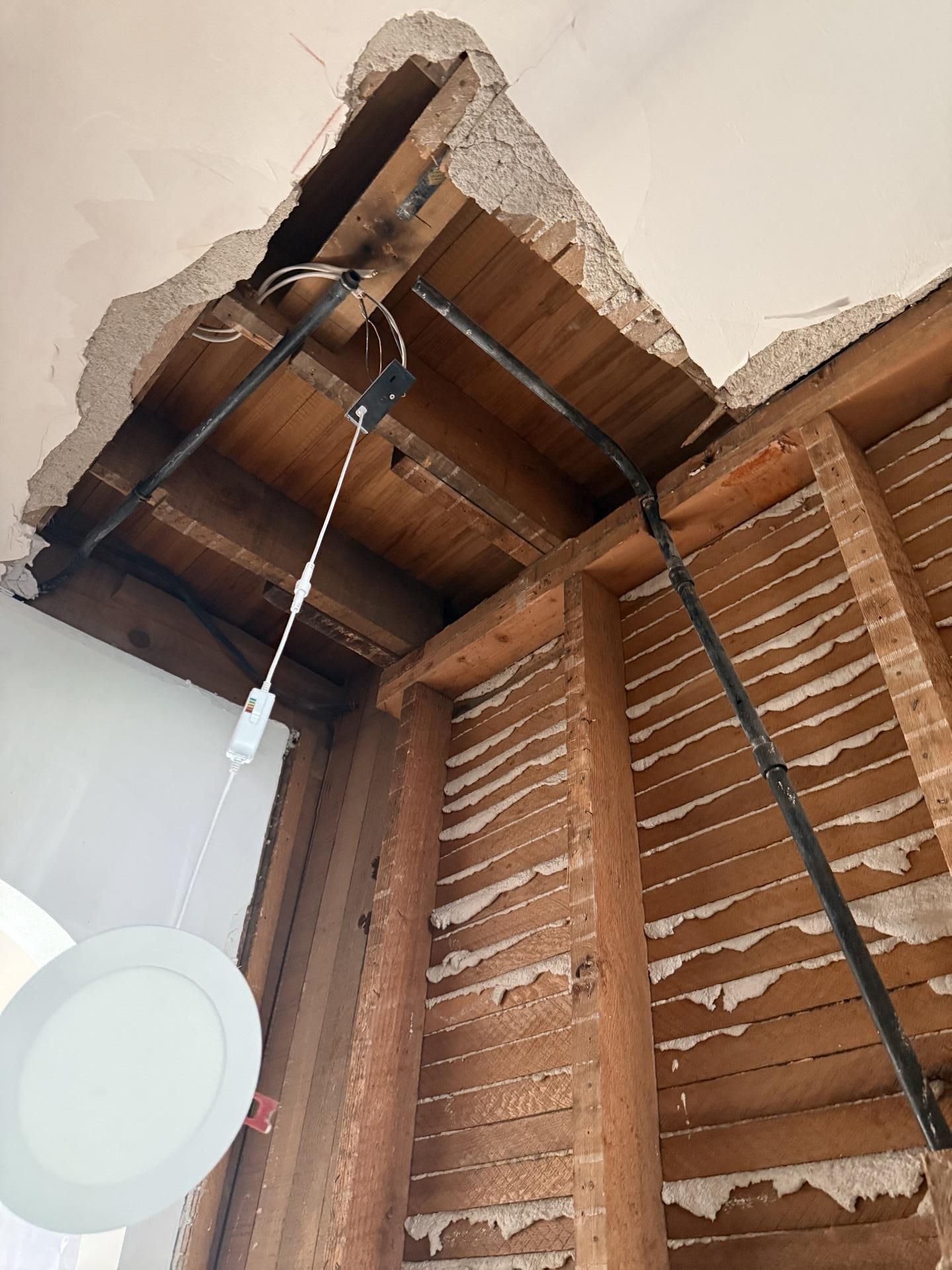 Exposed wooden ceiling with hanging light fixture and visible wiring in an unfinished room