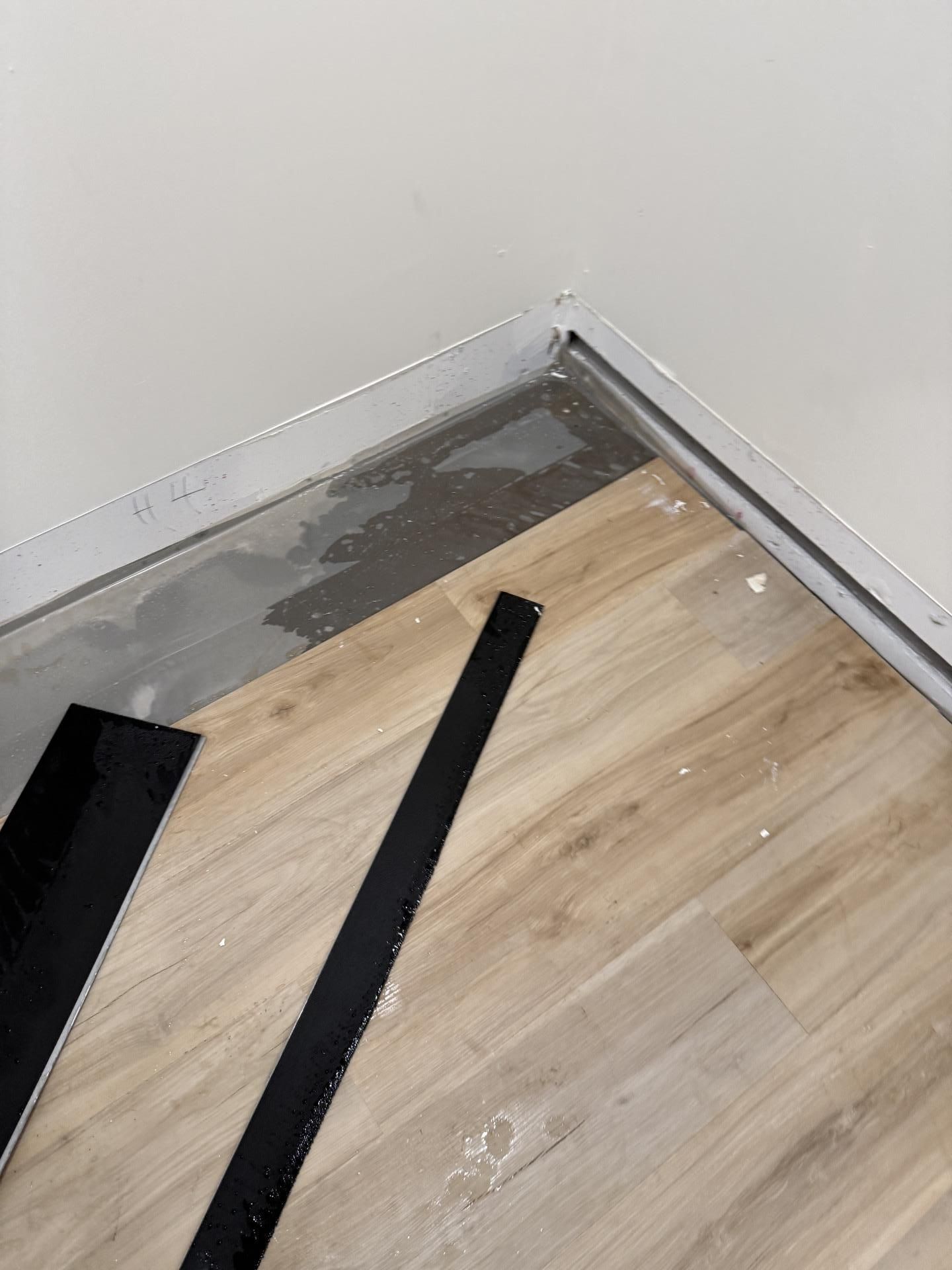 Corner of a room with unfinished flooring, gray underlayment, and two black strips on the floor.