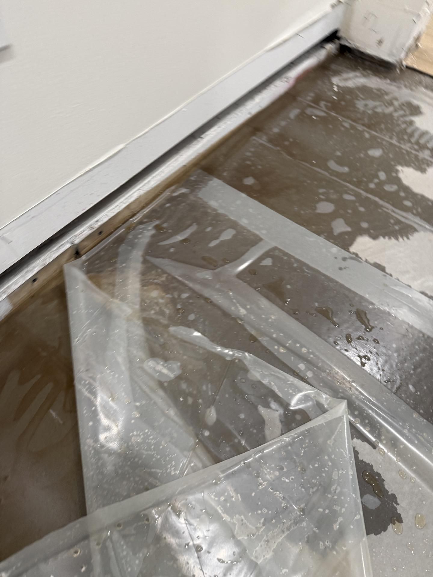 Plastic sheet covering a wet floor beside a wall and baseboard during cleanup