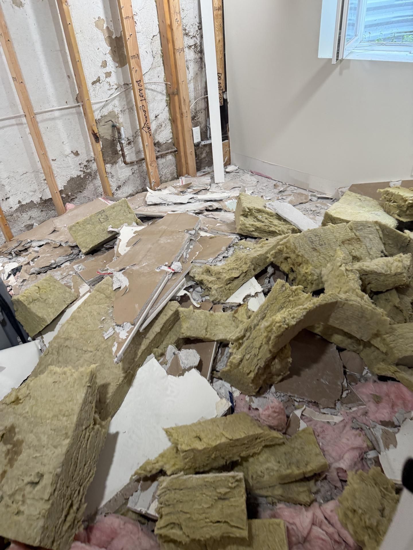 Damaged room with debris, broken drywall, exposed insulation, and rubble on the floor