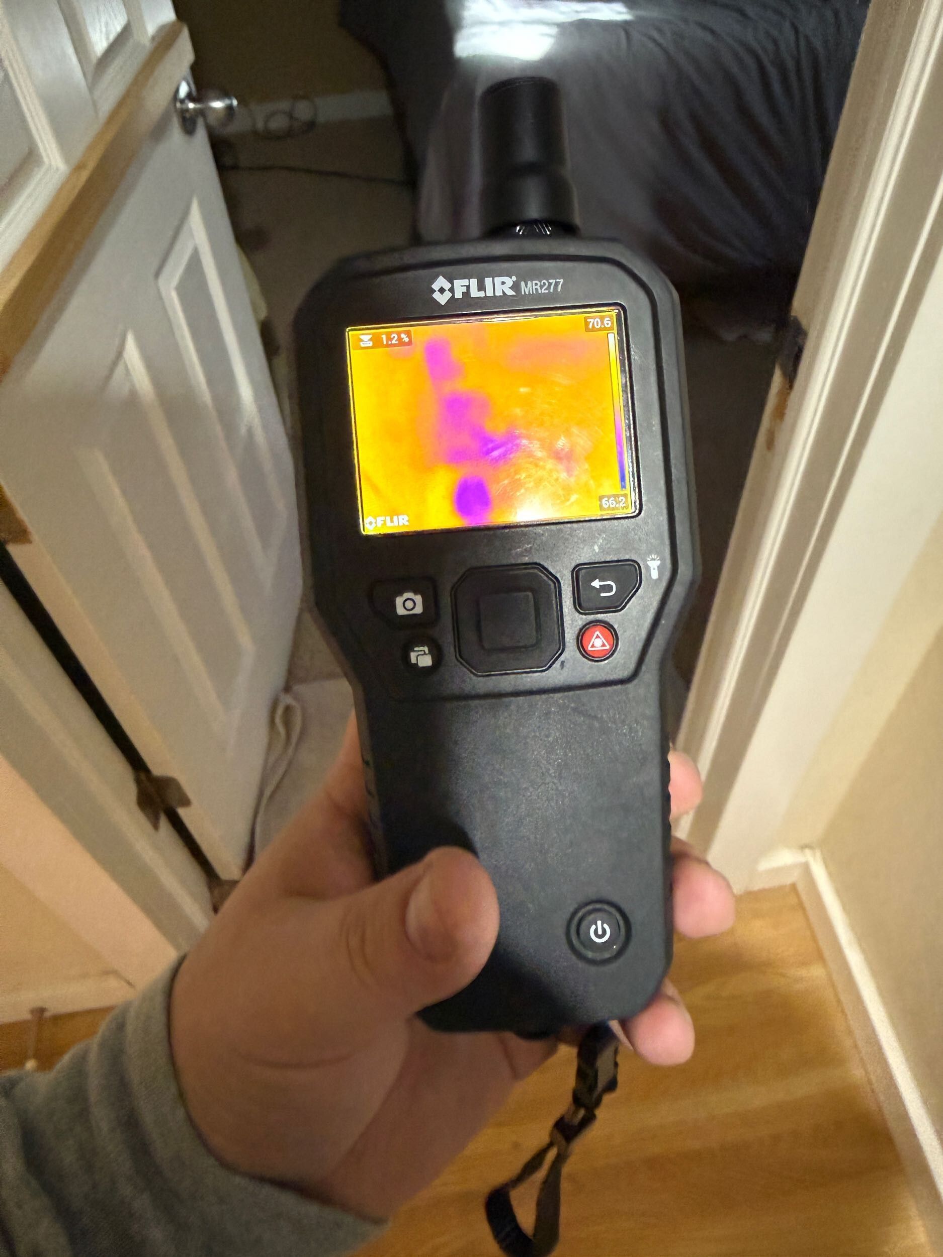 Handheld FLIR thermal camera displaying a heat map in a hallway doorway