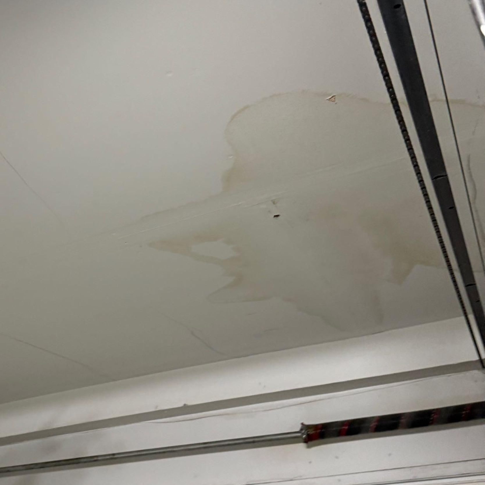 Water stain and peeling paint on a white ceiling near a metal frame.