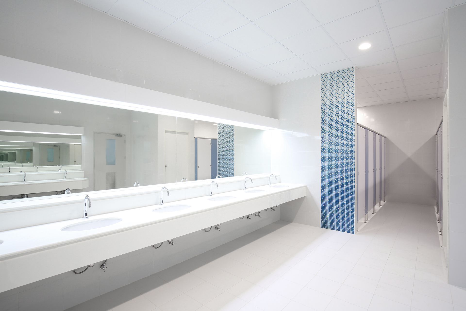 Bright modern restroom with long white sinks, mirrors, and blue tile accents