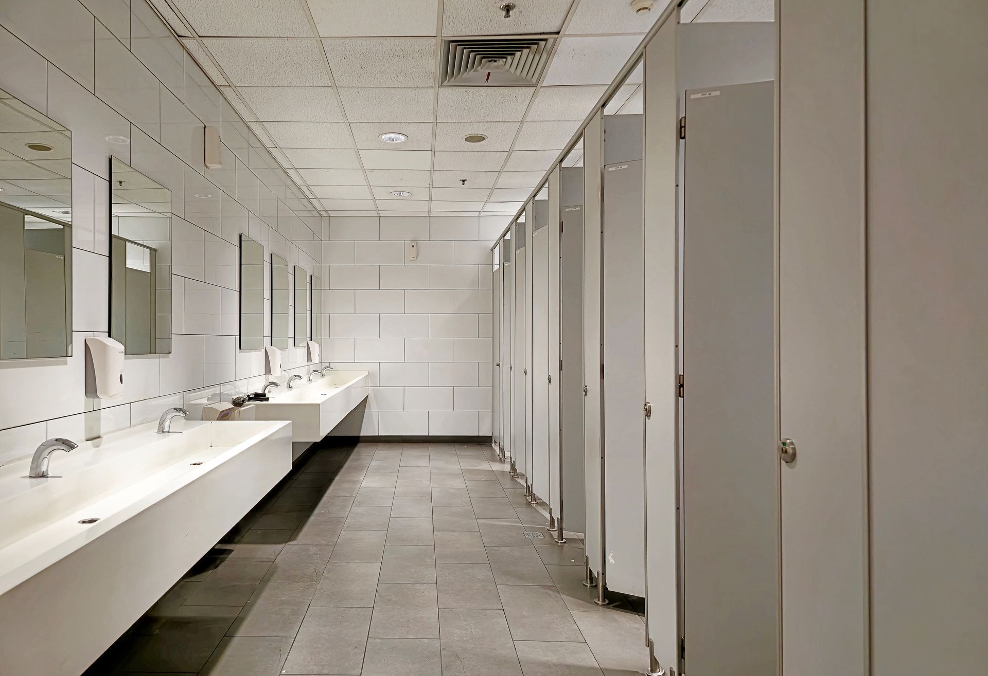 Empty public restroom with sinks on the left, stalls on the right, and tiled walls and floor.