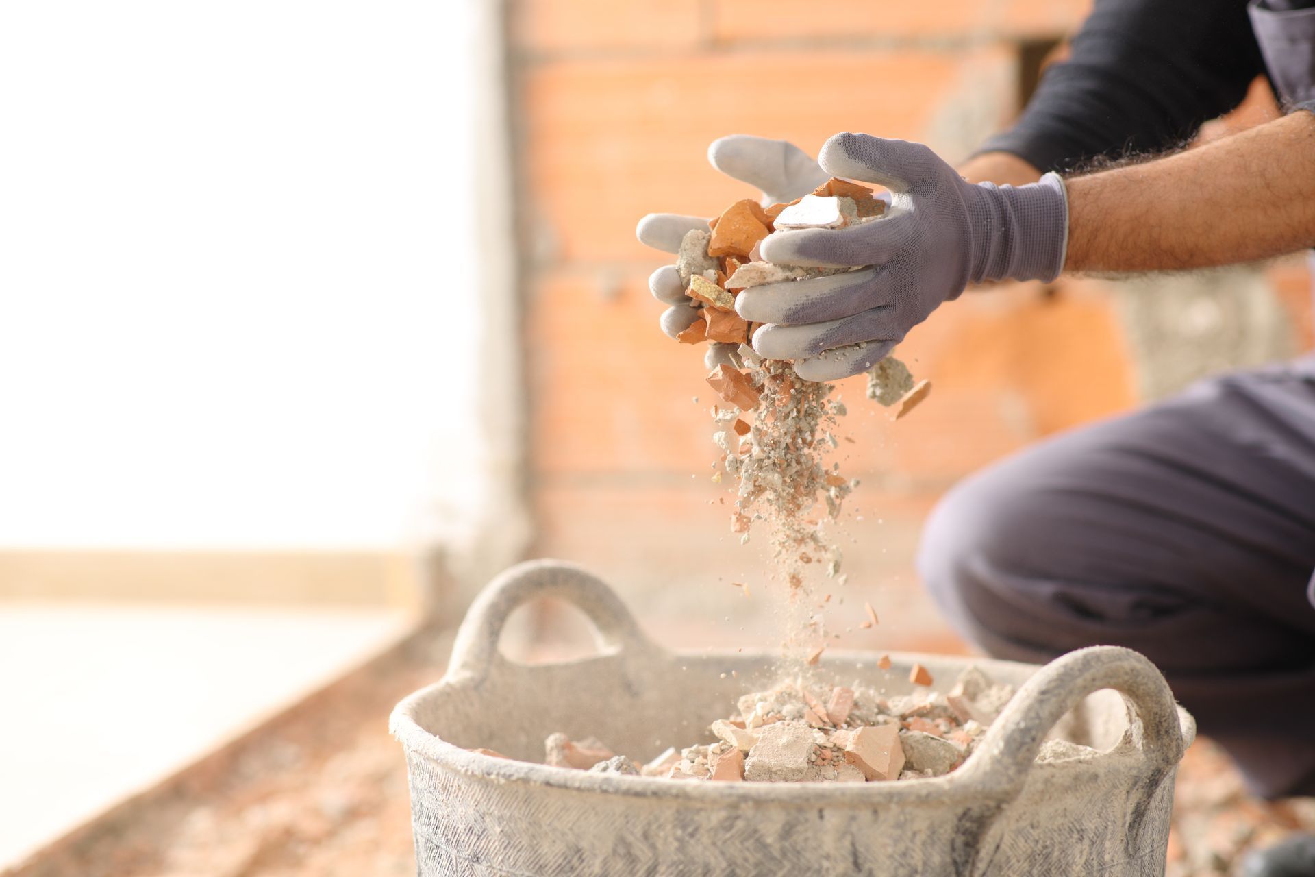 Gloved hands pour rubble into a gray bucket at a construction site