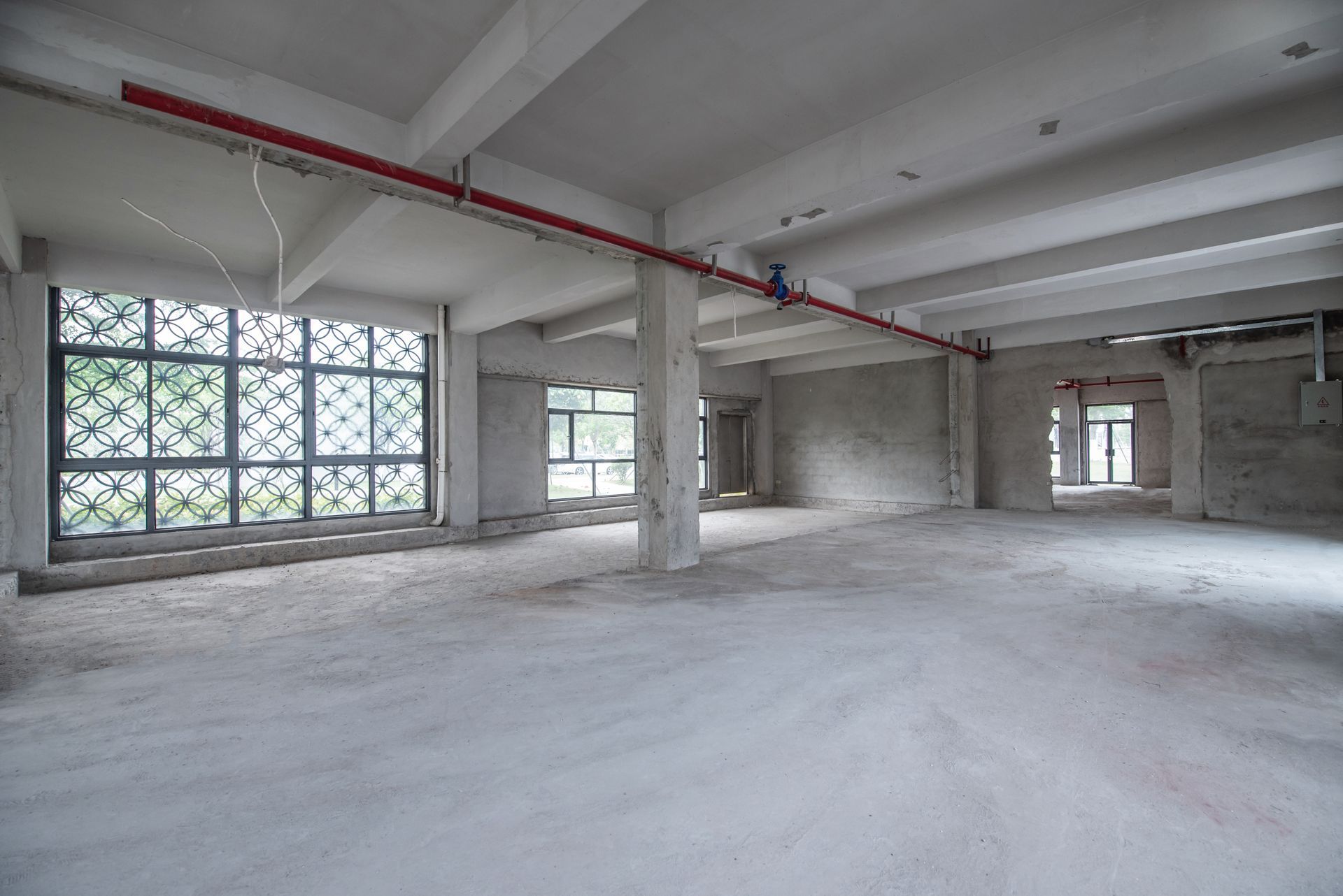 Empty unfinished concrete room with large windows and exposed ceiling pipes