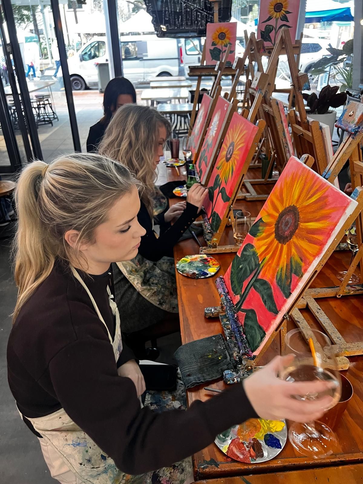 People painting colorful sunflower canvases at an art studio table