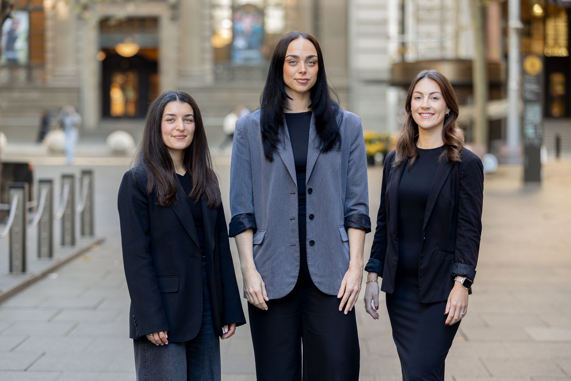 Three people in dark clothing standing outdoors in front of a building