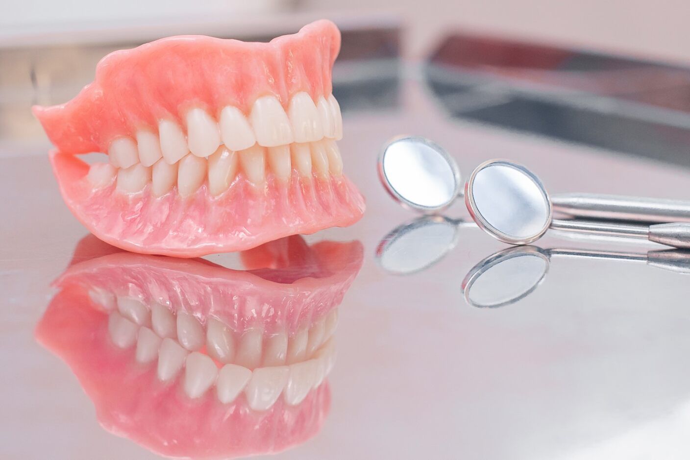 A Denture is Sitting on a Table Next to a Pair of Dental Mirrors — Jaw Gear Dental Prosthetics in Bowral, NSW