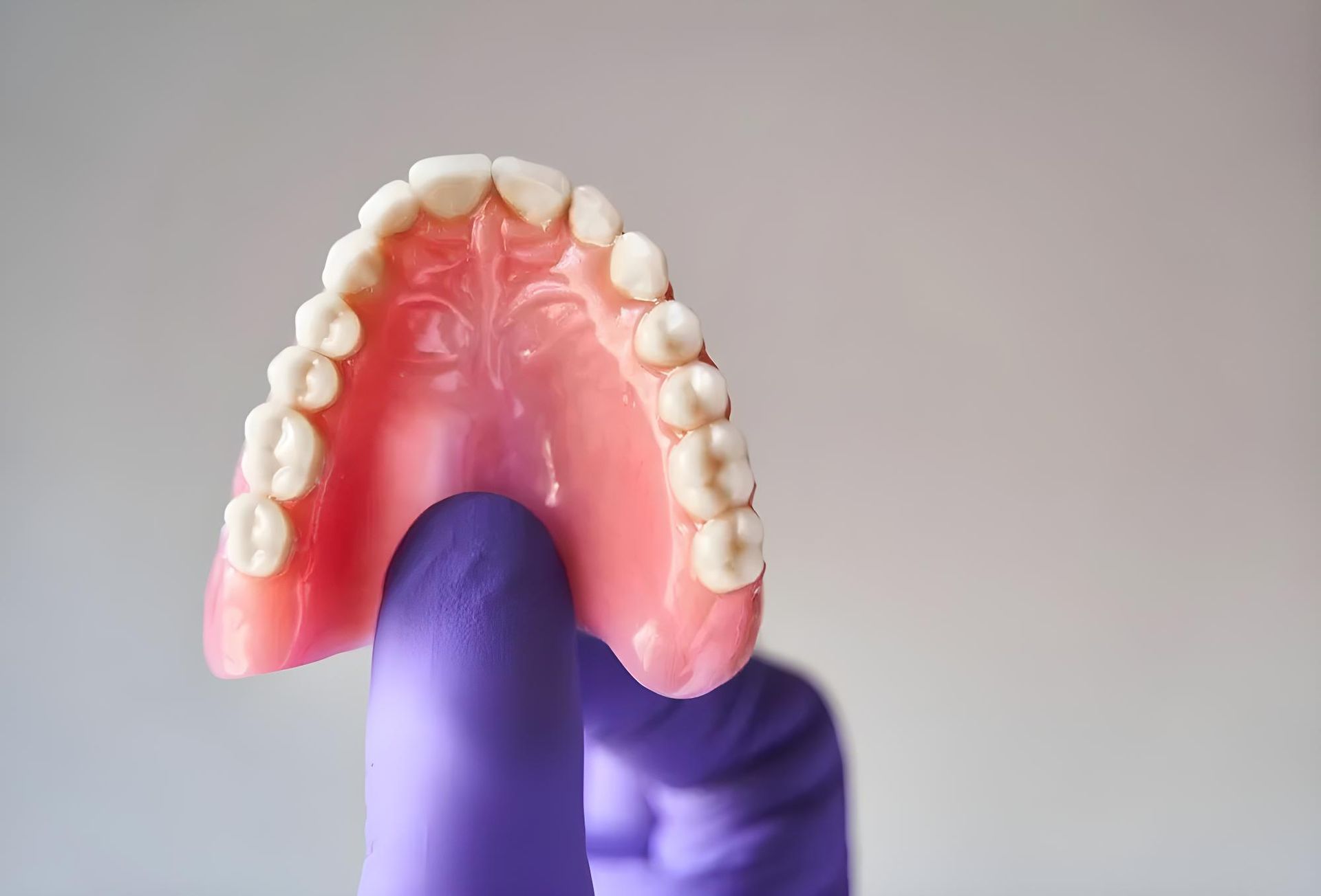 A Person Wearing Purple Gloves is Holding a Denture in Their Hand — Jaw Gear Dental Prosthetics in Bowral, NSW