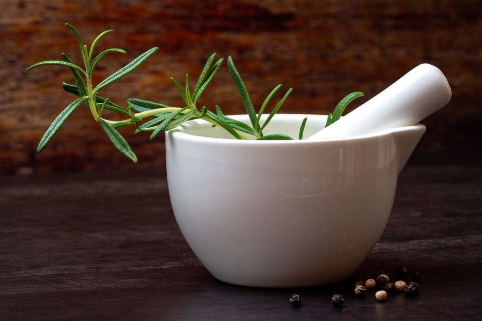 White mortar and pestle with green herbs on a dark wooden table