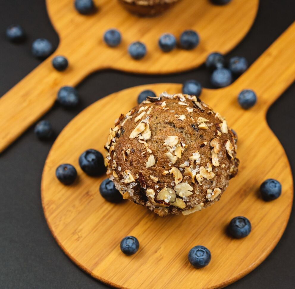 Oat and nut energy ball on a wooden spoon with scattered blueberries on a dark surface