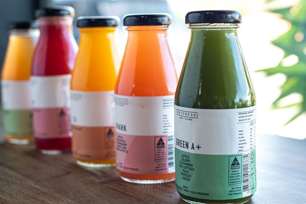 Colorful bottled juices lined up on a wooden table, with red, orange, and green drinks in focus.