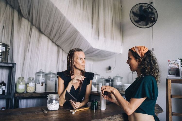 Two people talking at a café counter with jars and a clock on the wall