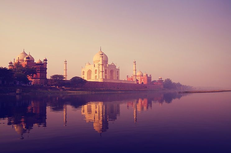 Taj Mahal at sunrise reflected in still water, with a pink and purple sky