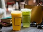 Two colorful smoothies in clear plastic cups on a table beside sunglasses and books