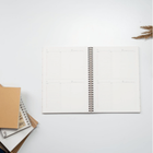 Open spiral notebook on a white desk with envelopes and papers at the left edge