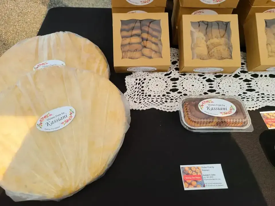 Cheese and packaged baked goods displayed on a black table with lace doily and business cards