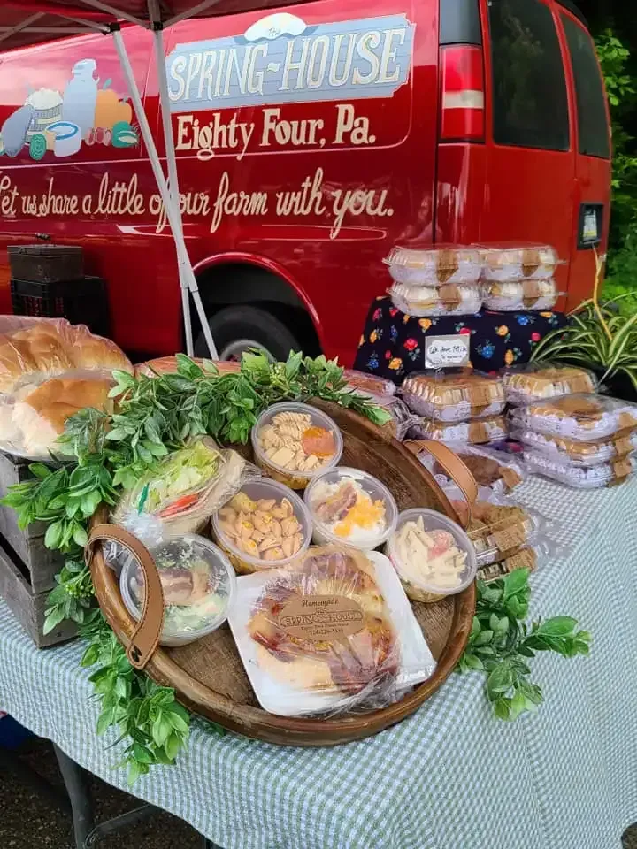 Catered food spread on a table with a red Spring House van in the background and a sign reading “Eighty Four, Pa.”