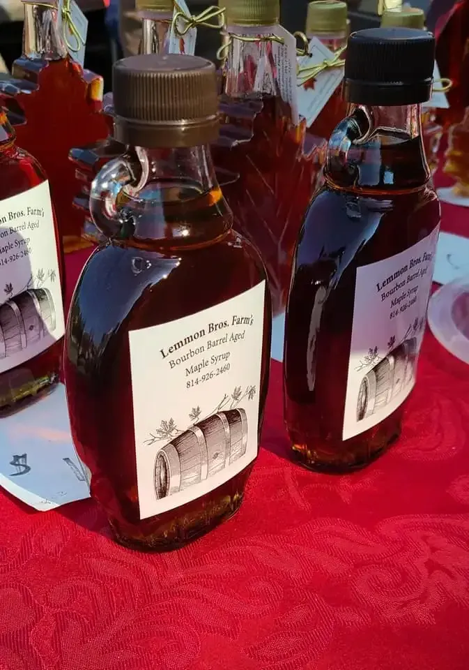 Glass bottles of dark amber liquid with labels on a red tablecloth at a market stall