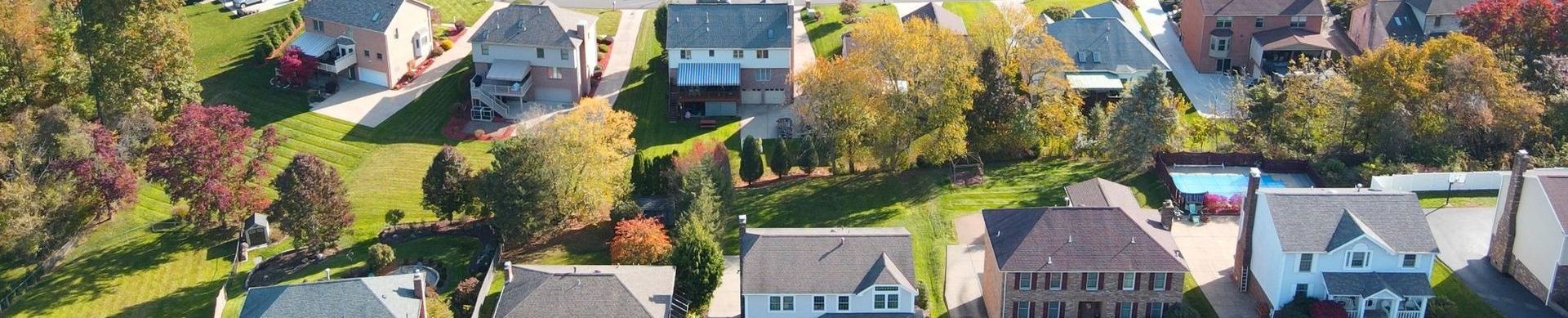 Aerial view of a suburban neighborhood with houses, trees, and fall-colored foliage along a curving street