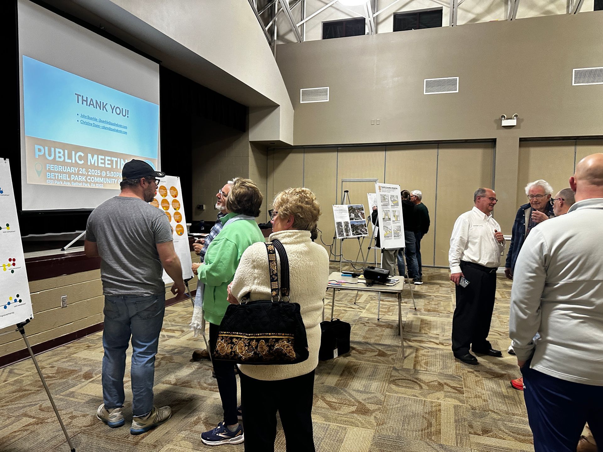 People mingling at a conference poster session in a large lobby with presentation boards and a blue screen.