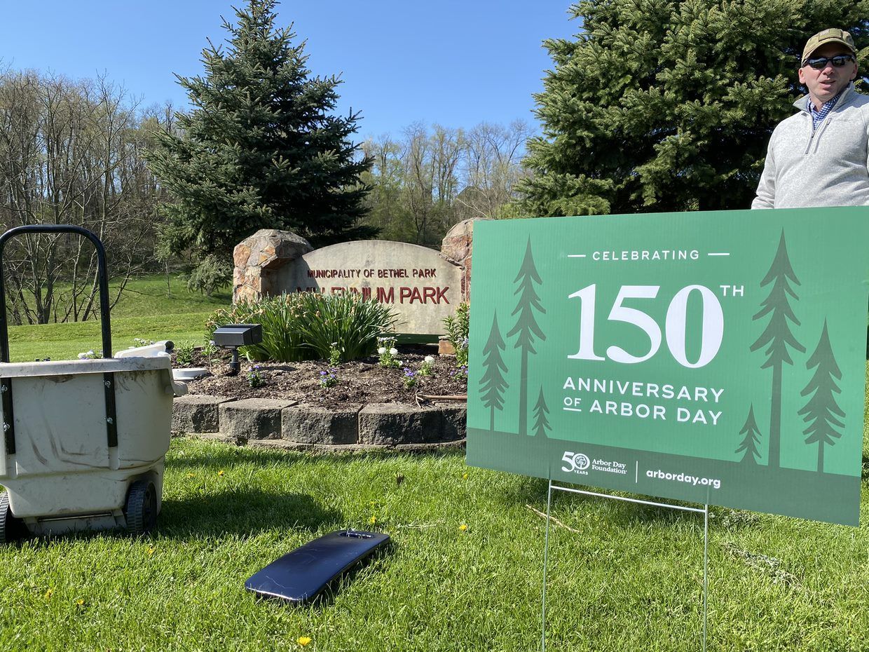 Sign for Celebration of the 150th anniversary of Arbor Day in a grassy park, with a person standing nearby
