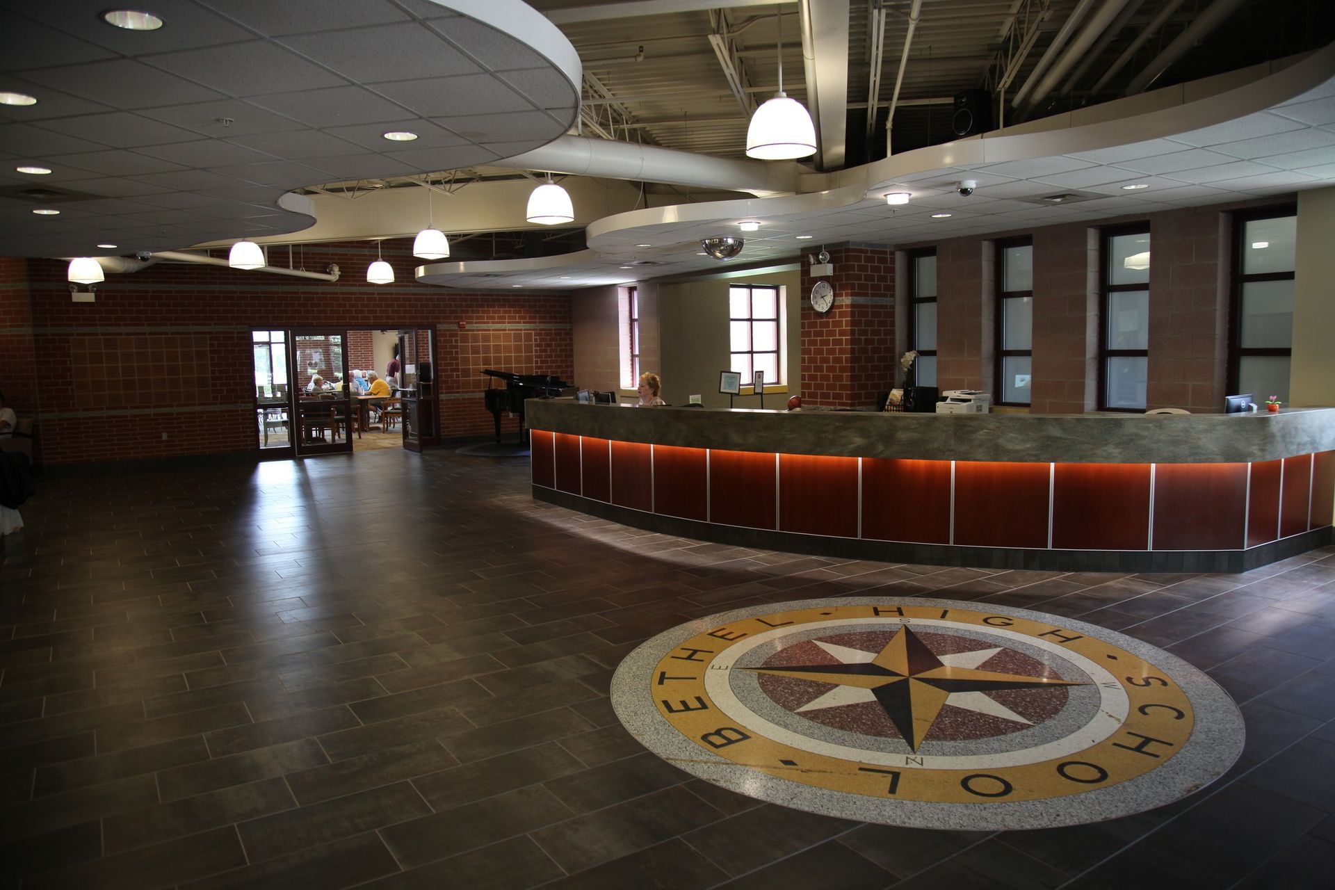 Empty lobby with curved reception desk, dark floor, hanging lights, and compass mosaic in the foreground