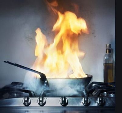 Kitchen pan on a gas stove engulfed in flames, with smoke and a bottle nearby