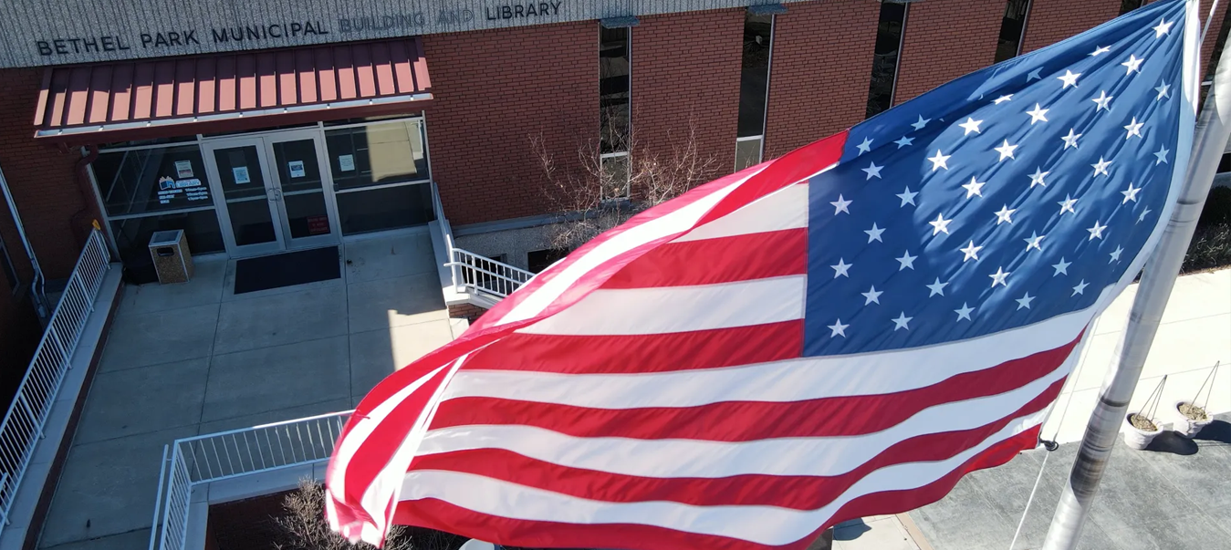 Large American flag waving in front of a brick building entrance with a red awning