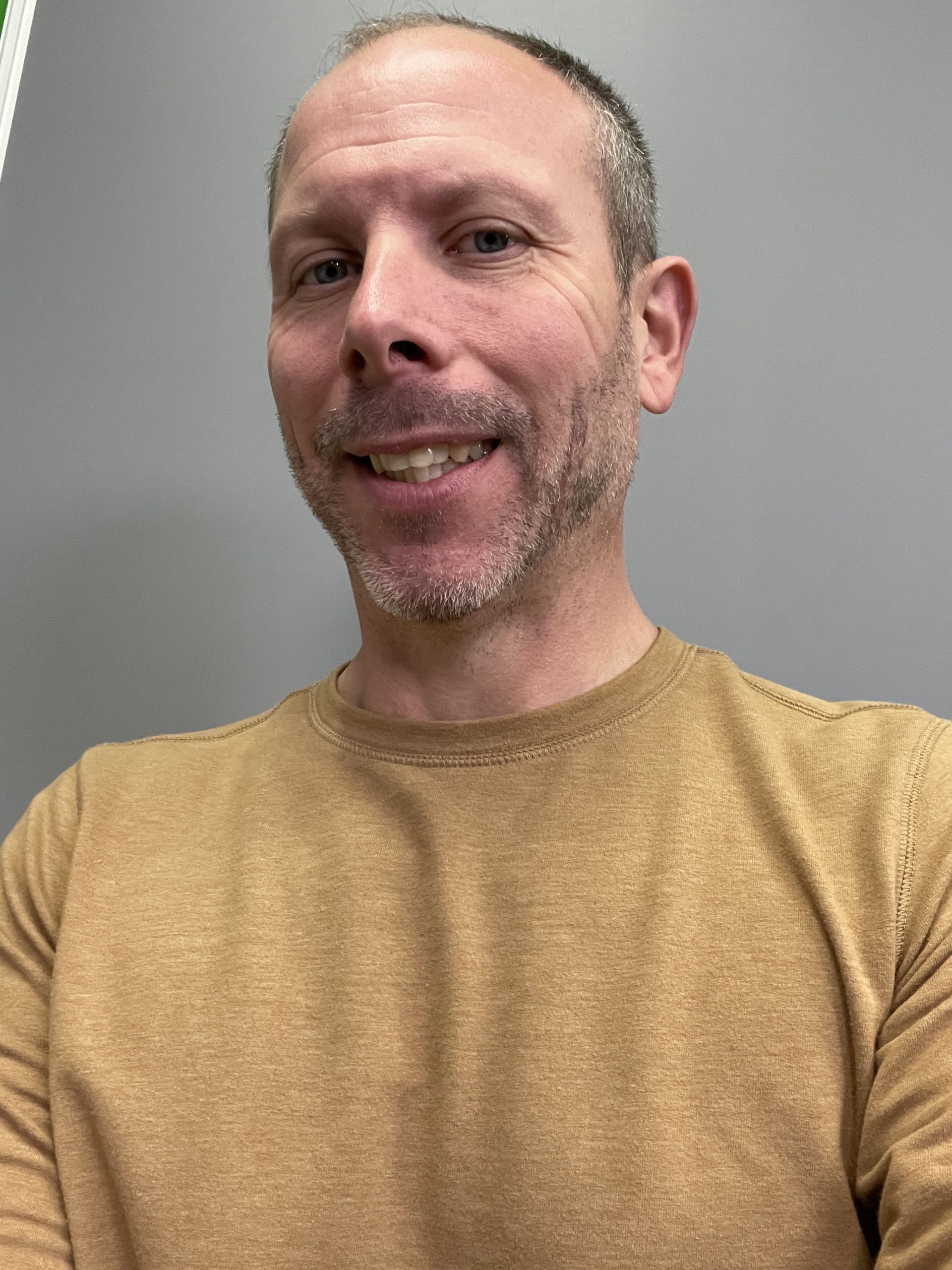 Smiling person in a mustard shirt against a plain gray background