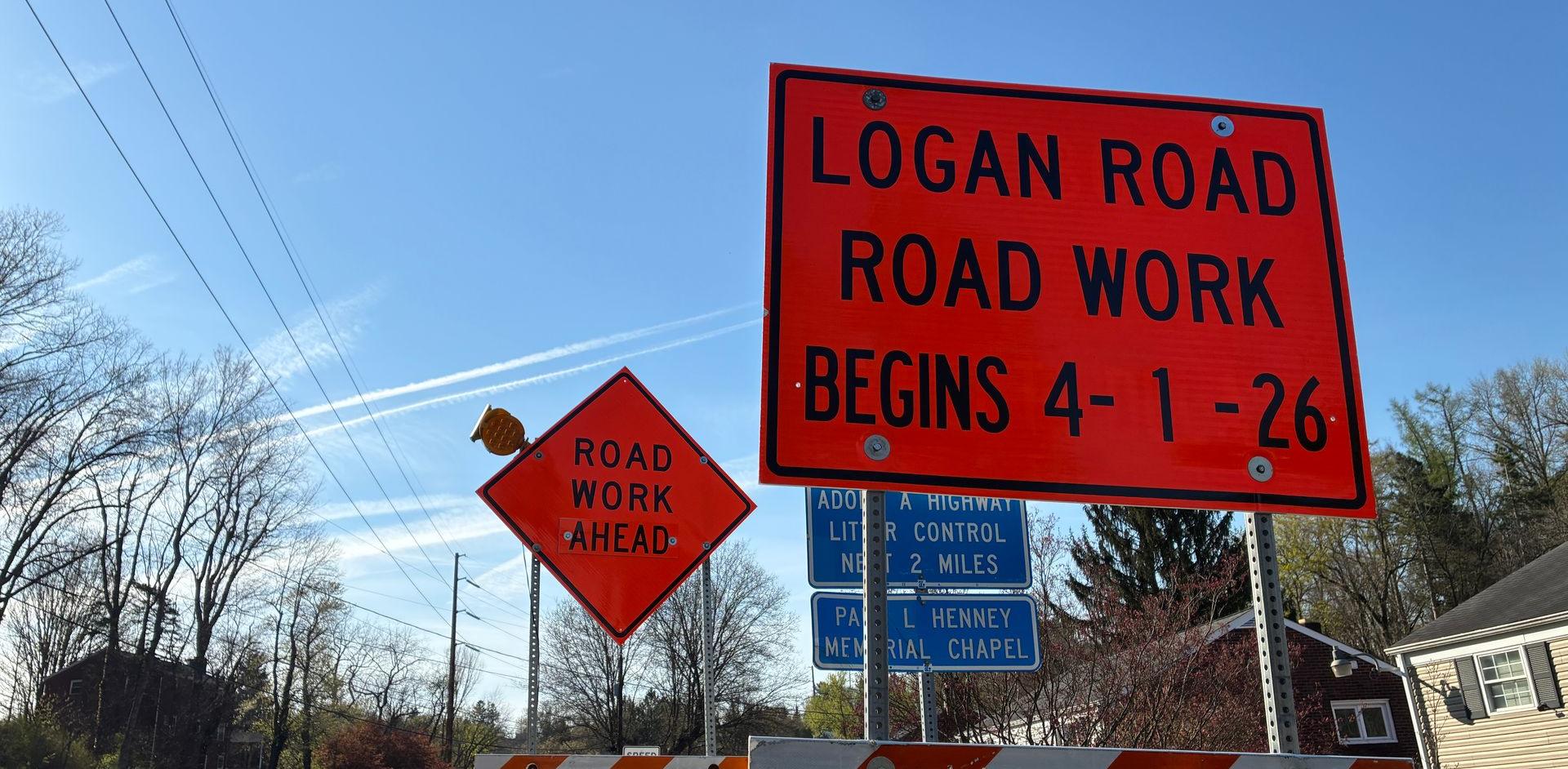 Red road work sign on Logan Road; orange sign warns work begins 4-1-26.