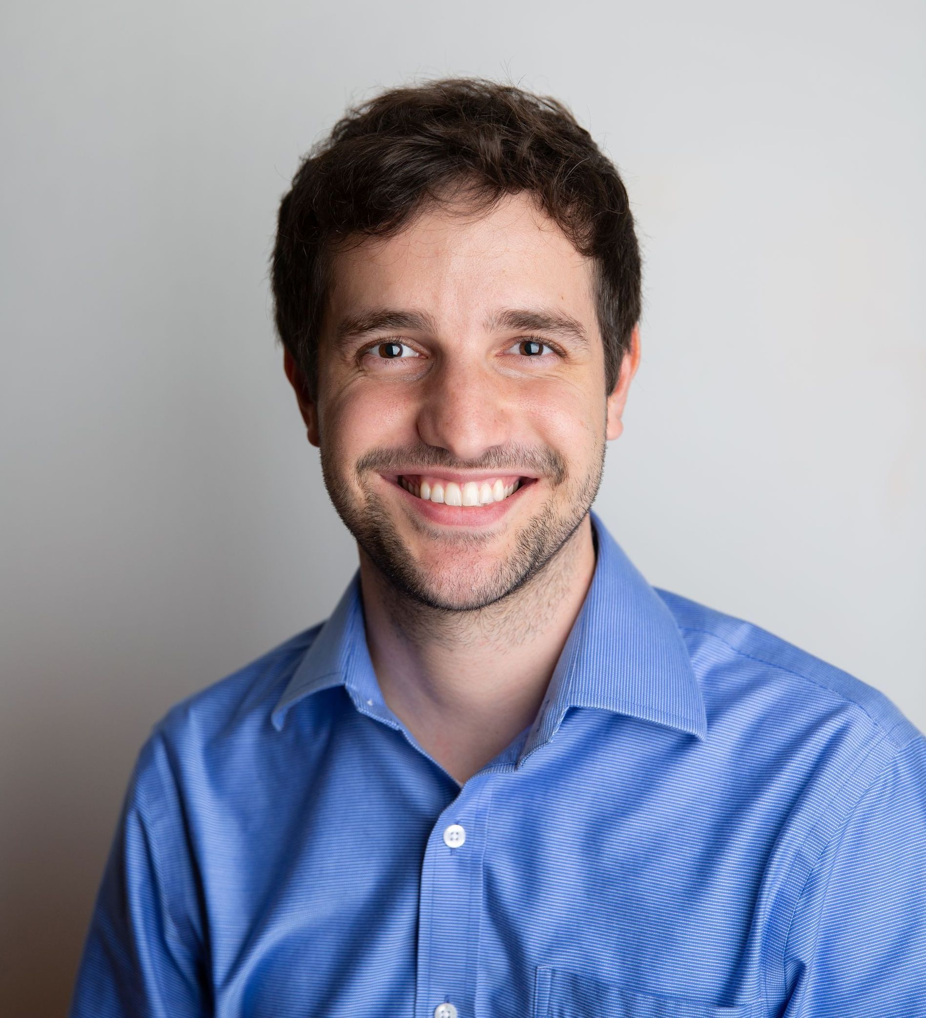 Smiling man in a blue shirt against a light gray background