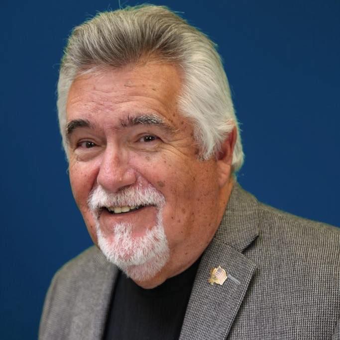 Smiling man in gray blazer and black shirt against a blue background