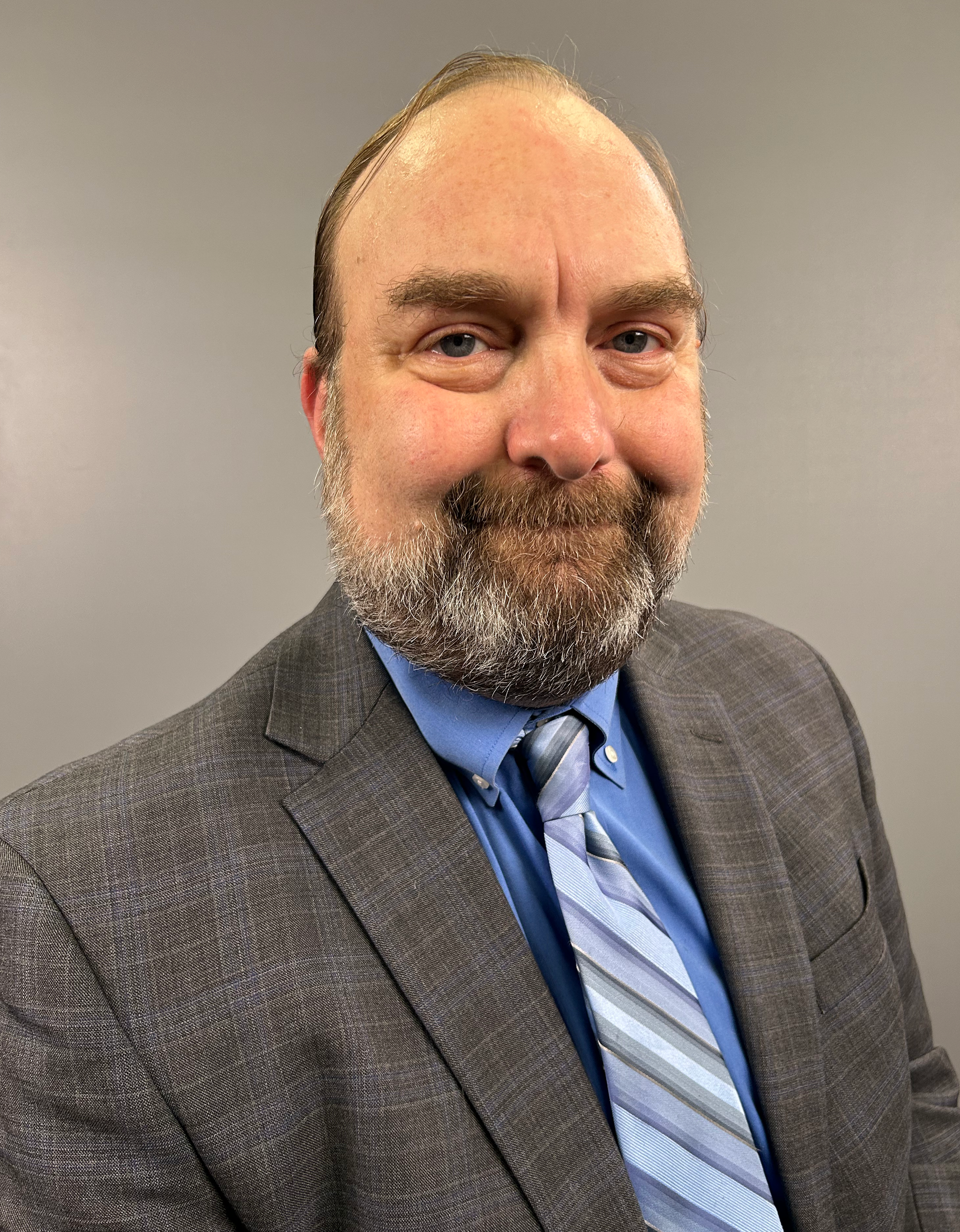 Man in a gray suit and blue tie smiling against a plain gray background