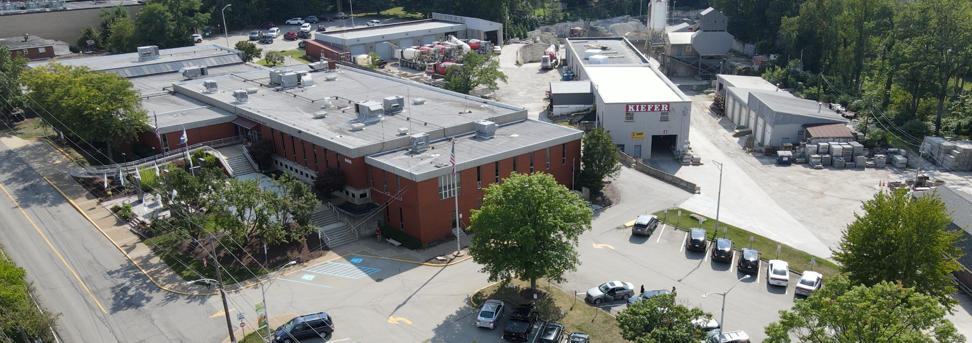 Aerial view of a brick building and parking lot with trees and parked cars