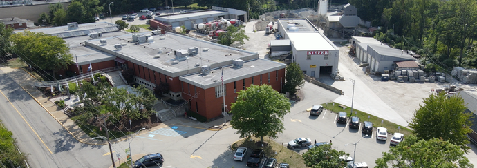 Aerial view of a brick commercial building with parking lots and surrounding trees on a sunny day