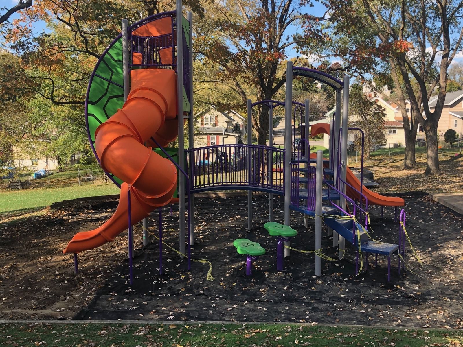 Empty playground with orange spiral slide, climbing structure, and mushroom seats in a leafy park