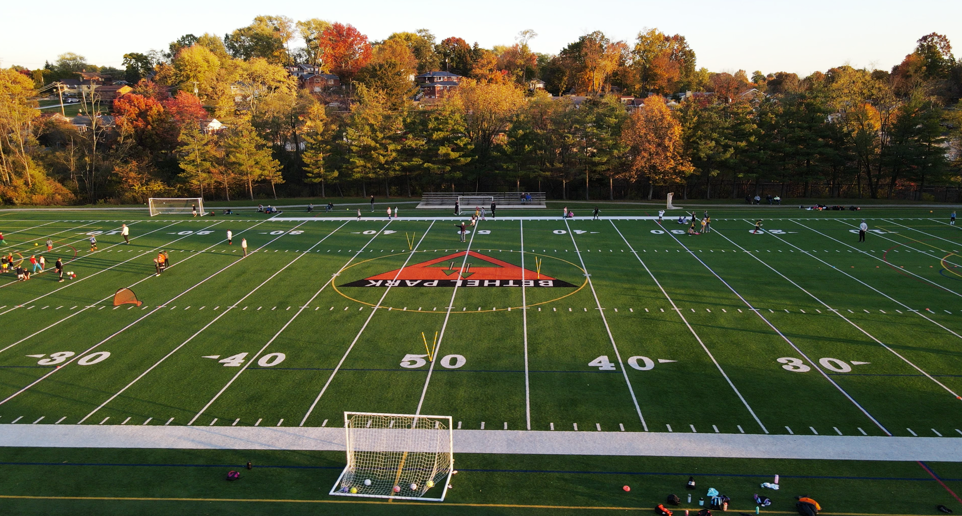 Empty soccer field with white lines and goal, viewed from above with autumn trees in the background