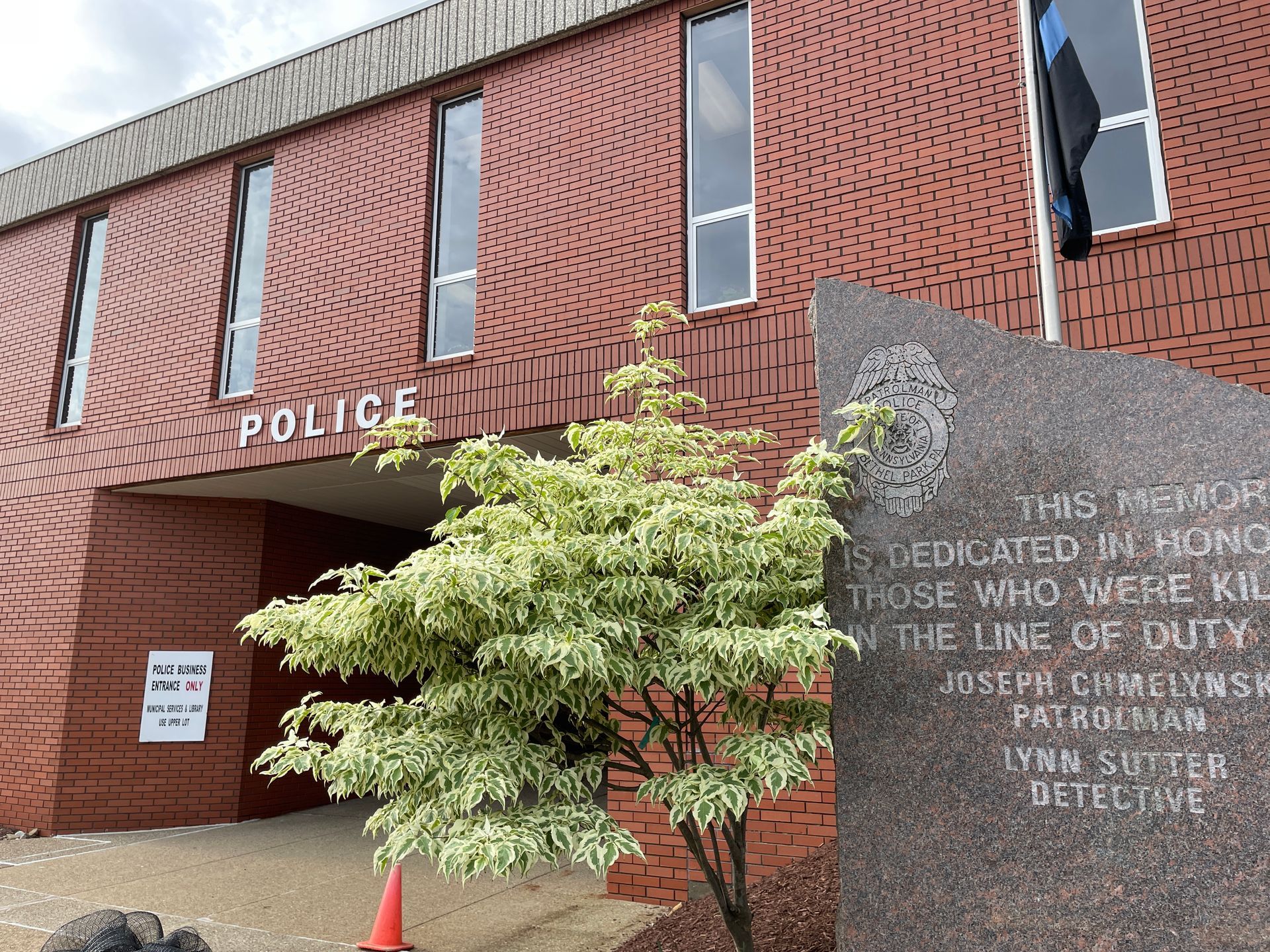 Police station entrance with red brick facade, black windows, and a small tree in front
