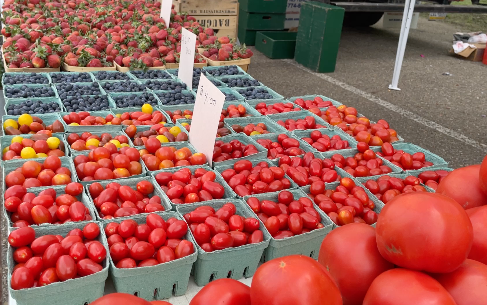 Tomatoes and berries in crates at an outdoor market stall