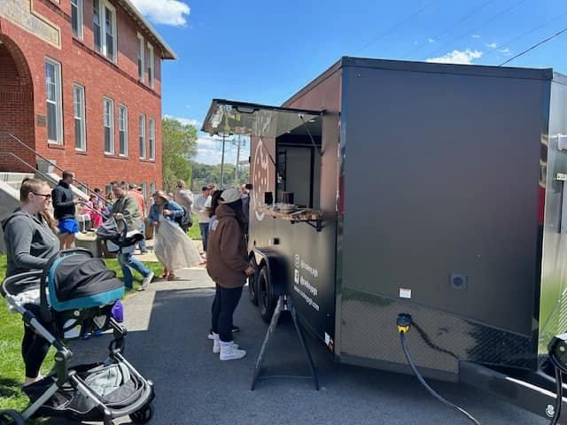 Outdoor food truck service beside a brick building, with people waiting and a stroller in the foreground.