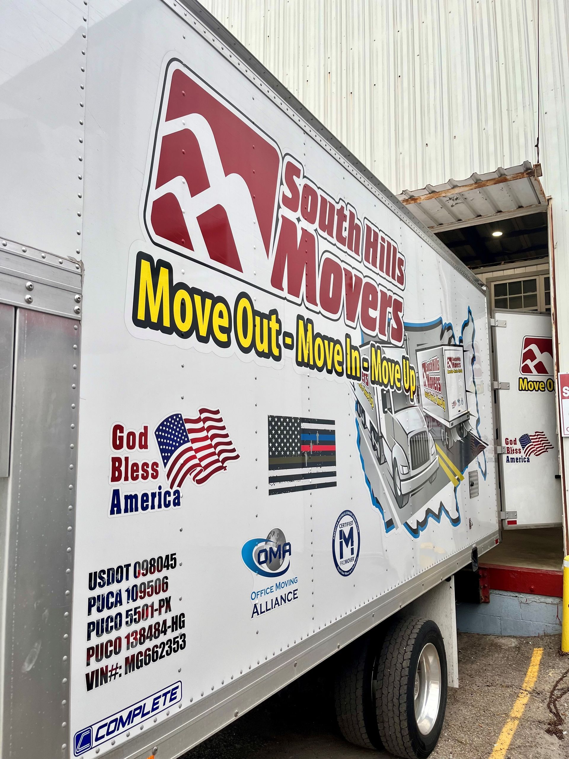 Moving company truck with red, white, and yellow branding parked at a loading dock near a building.