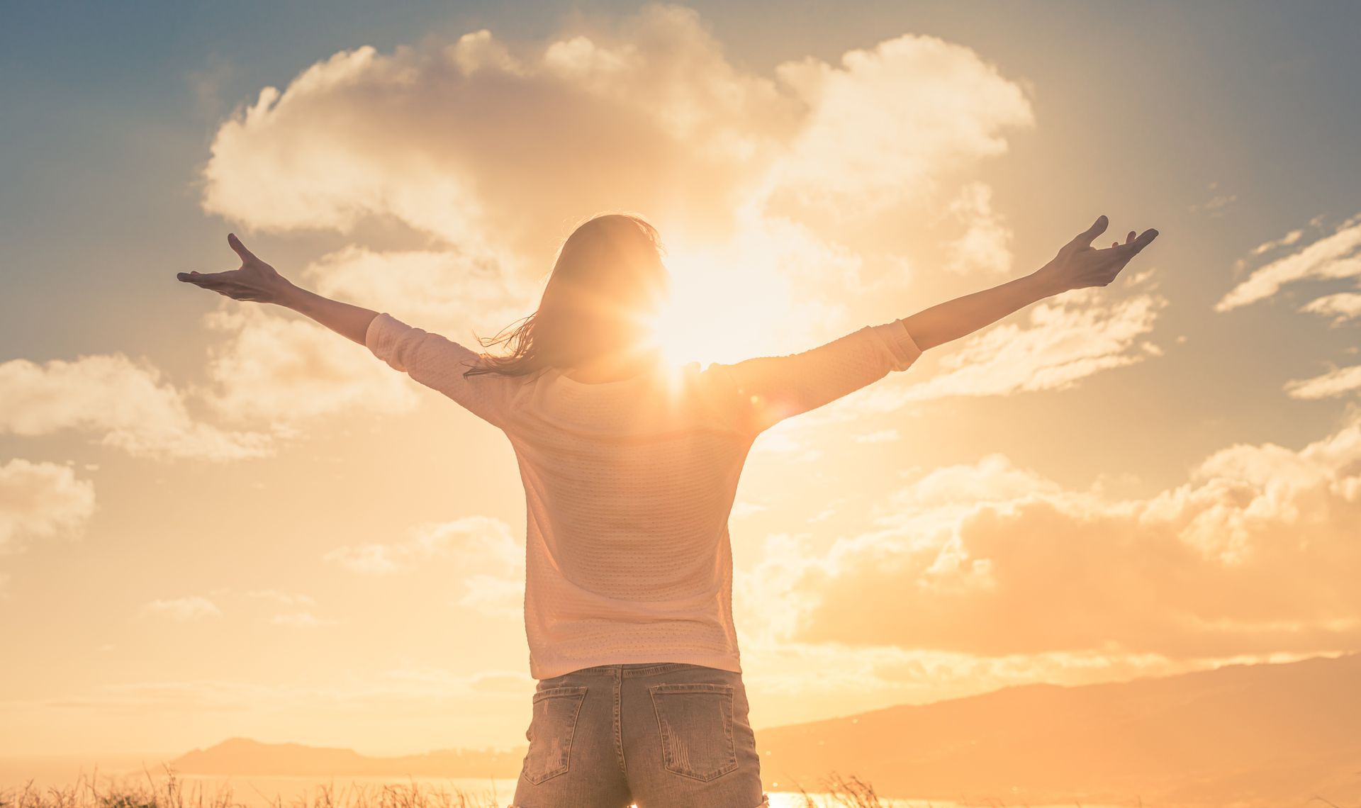 Person standing with arms raised toward a bright sunset sky