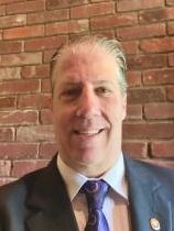 Smiling man in a suit and tie standing before a brick wall