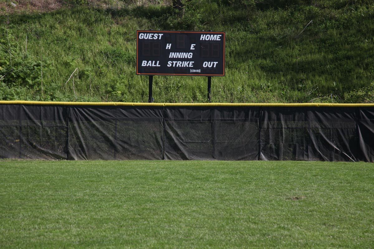 Baseball outfield with a black scoreboard behind a yellow-topped fence and green grass foreground
