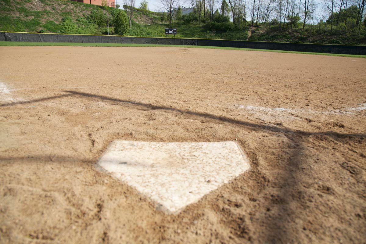 Baseball home plate on a sandy infield with trees and a grassy hill in the background