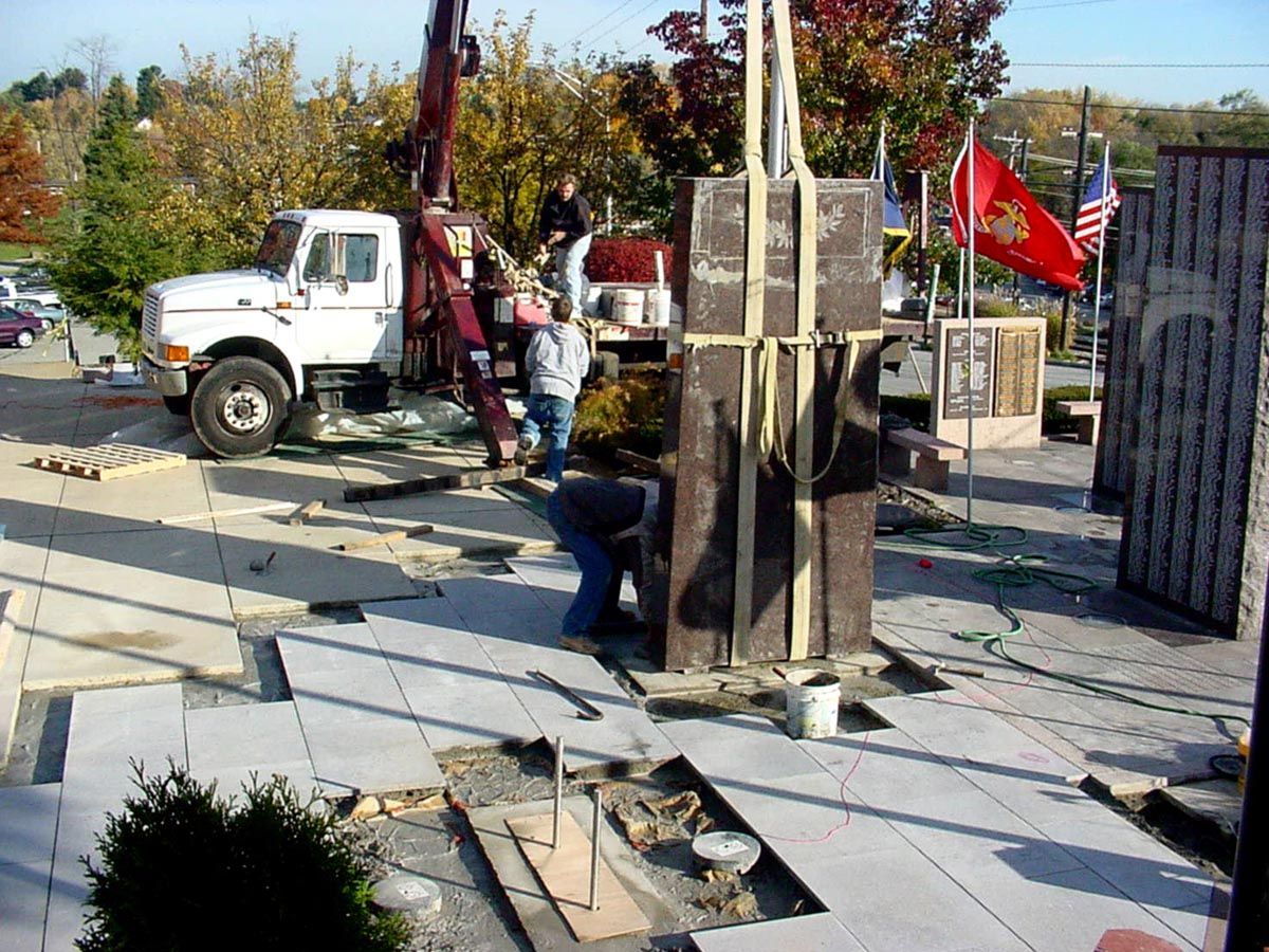 Truck and workers beside a damaged monument or sculpture in a plaza, with debris scattered on the ground