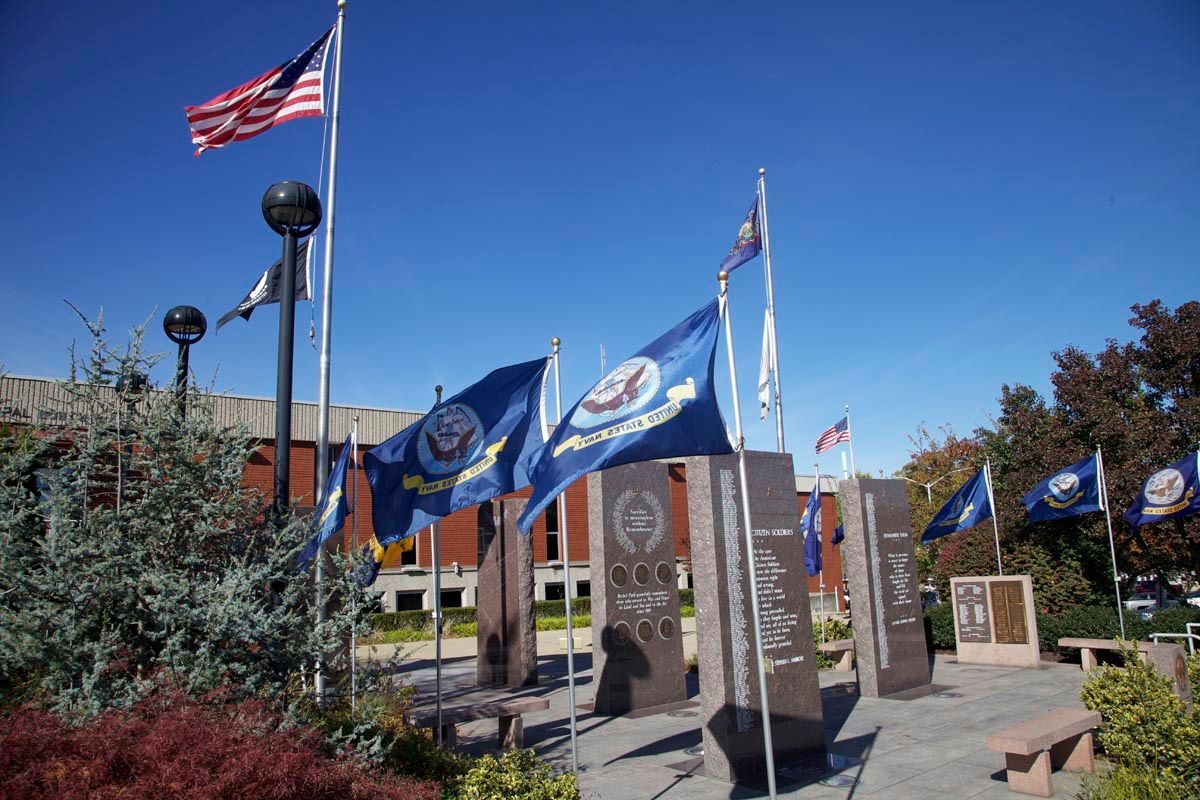 Memorial plaza with flagpoles, blue flags, and stone pillars under a clear sky