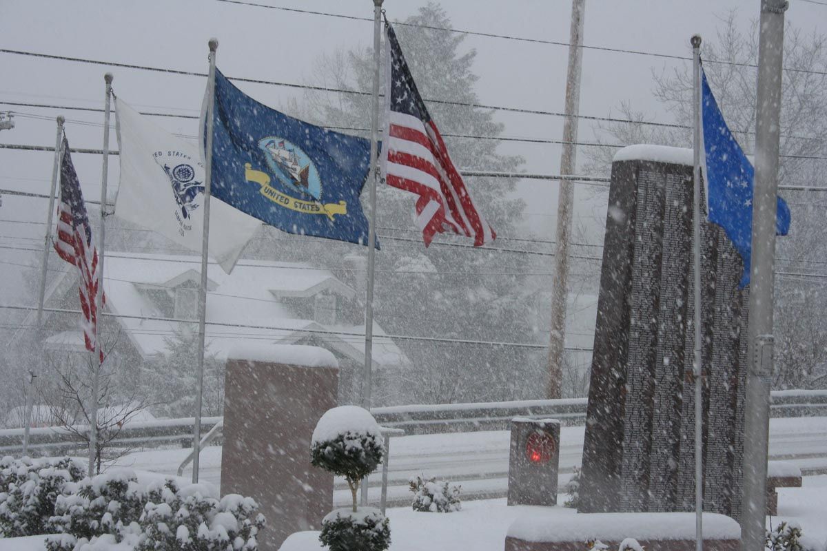 Snowy outdoor scene with U.S. and state flags waving near a building and parking lot